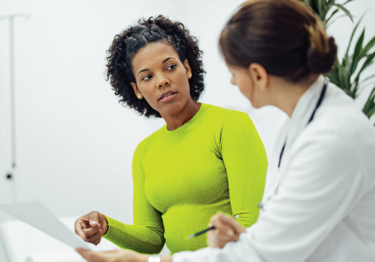 Actor portrayals of female patient in green shirt talking to female doctor, pointing to Doctor Discussion Guide