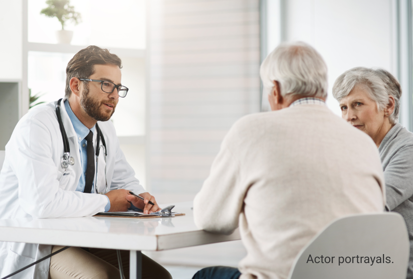Actor portrayals of male doctor with glasses and a stethoscope around his neck sitting at a table and talking to a male and female patient