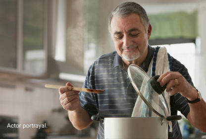 Actor portrayal of man in striped polo shirt lifting lid off of pot and holding wooden spoon