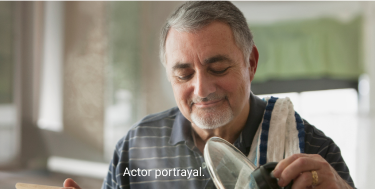 Actor portrayal of man in striped polo shirt lifting lid off of pot and holding wooden spoon