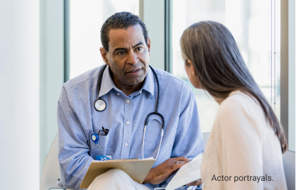 Actor portrayals of male doctor with stethoscope around his neck sitting with female patient while discussing documents